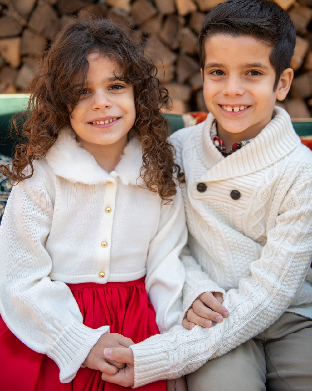 Two children in white sweaters sitting together, one wearing a red skirt.