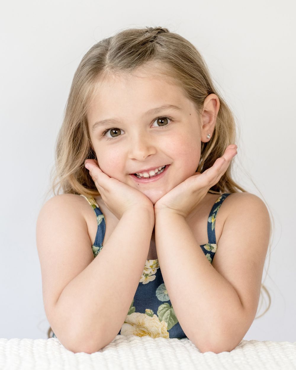 Studio portrait of child in floral dress with hands under chin.