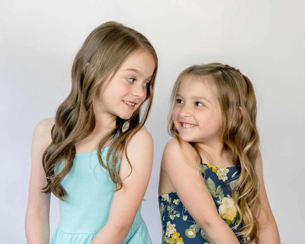 Two children in casual dresses sharing a moment against white background.