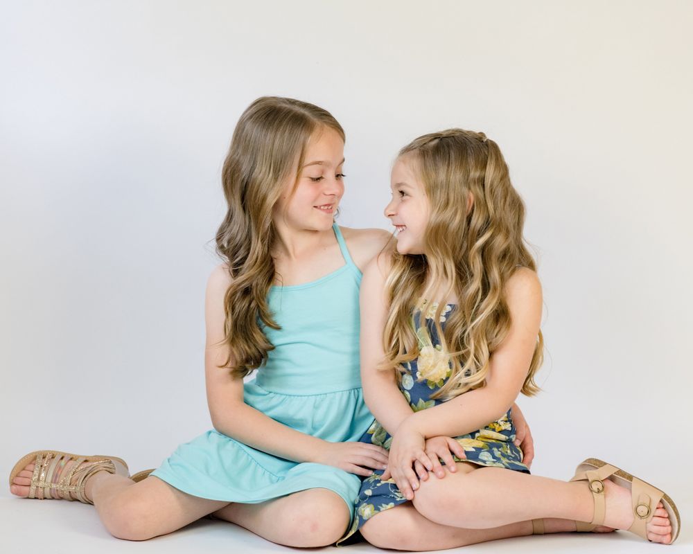 Two children in casual dresses sitting together on white background.