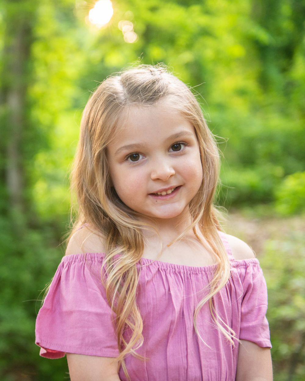 Outdoor portrait in pink off-shoulder dress with natural forest background.