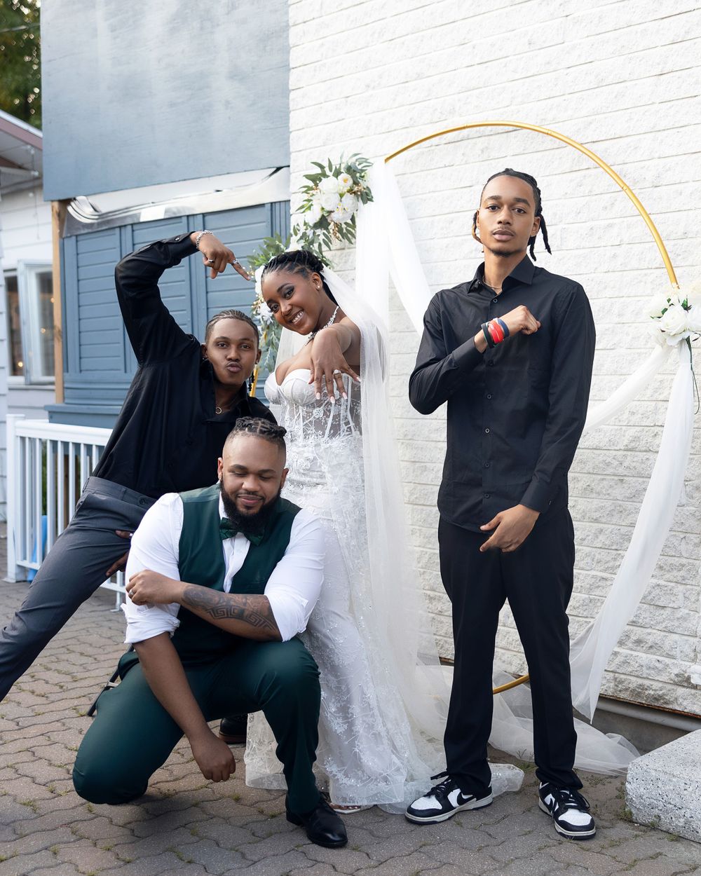 A wedding party posing playfully against a white wall with decorative arch.