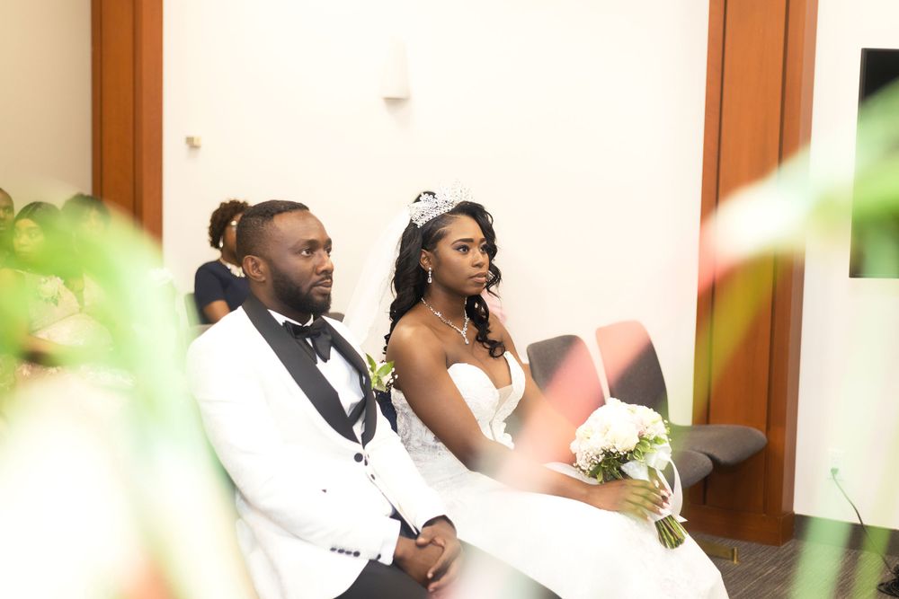 Newlyweds seated together during wedding ceremony with soft focus greenery.