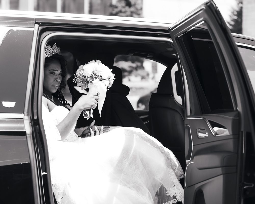 Bride holding white bouquet while seated in luxury car.