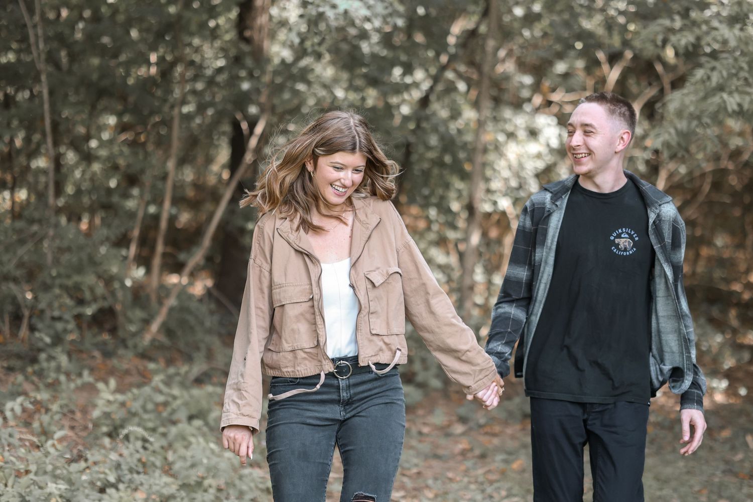 Couple walking and laughing together on a wooded path in autumn.