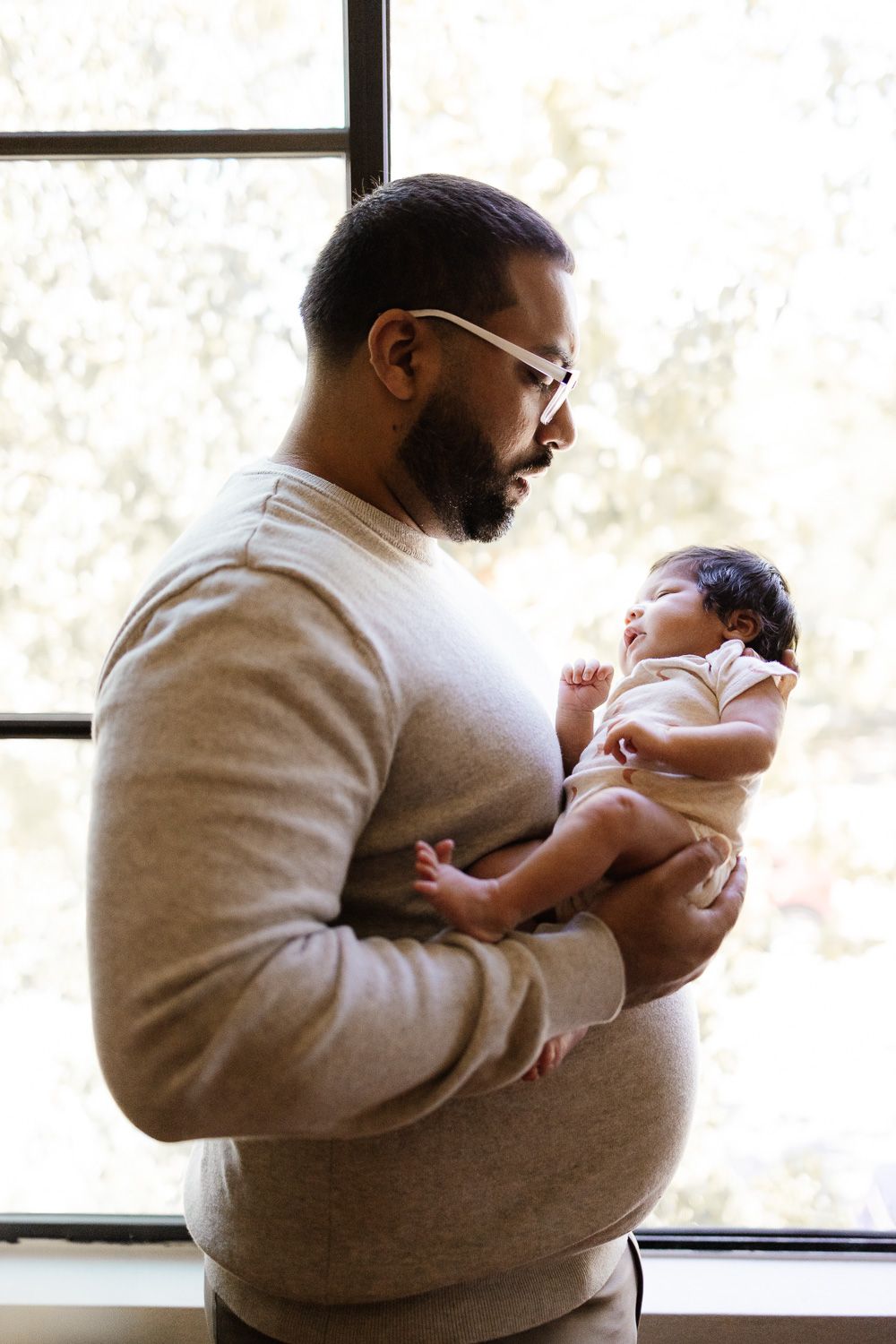 Dad holds baby by window at San Jose in-home lifestyle newborn photoshoot by San Jose Newborn Photographer Cindy Tucey