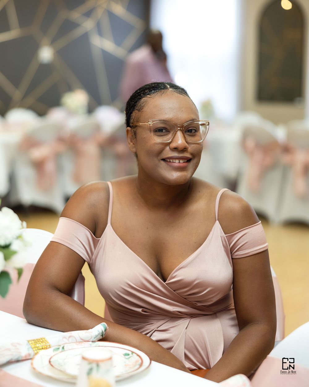 Portrait of someone in pink formal dress seated at decorated table setting.