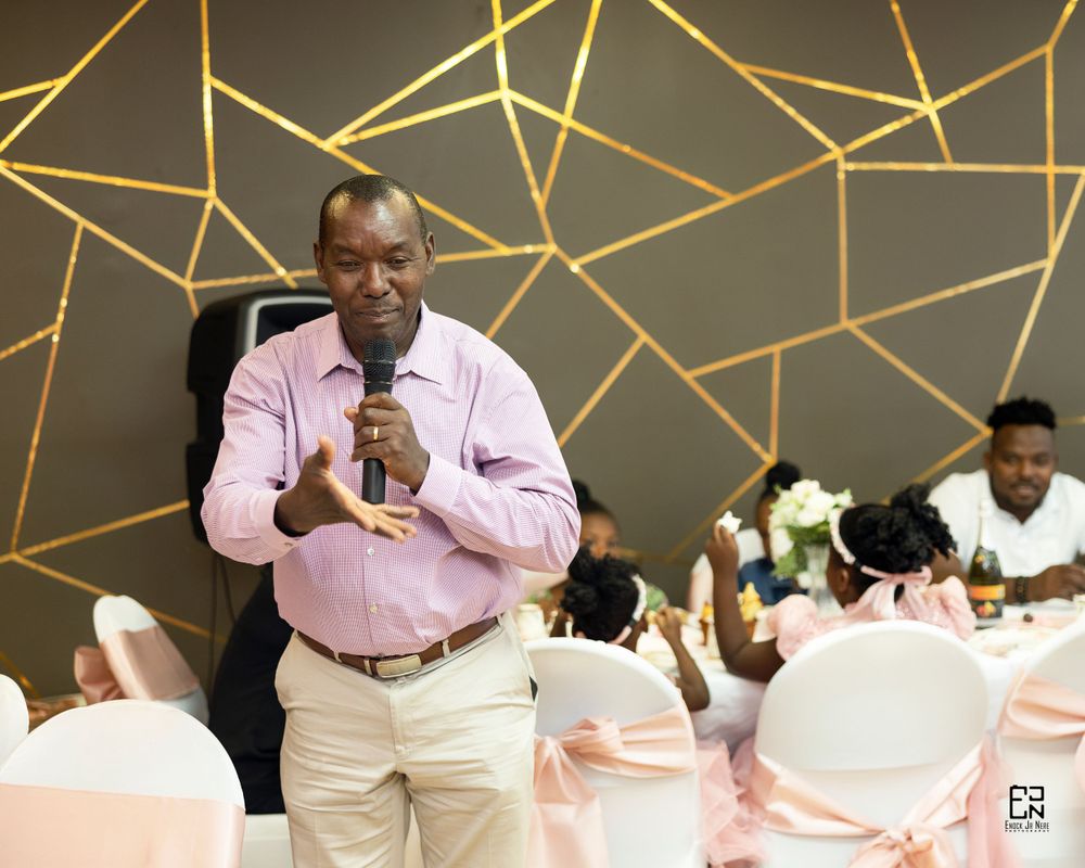 Speaker addressing guests during a celebration with geometric wall art and pink decor.