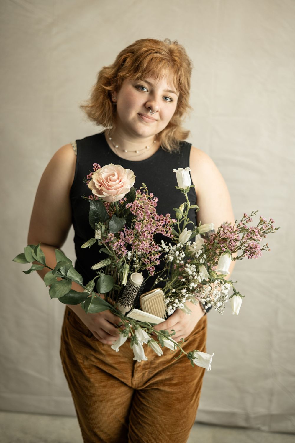Model in brown pants poses with floral arrangements featuring roses and wildflowers against neutral backdrop.