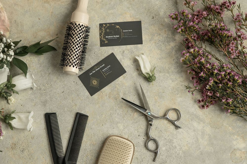 Professional hair styling tools and products arranged on textured gray surface with delicate pink floral accents.