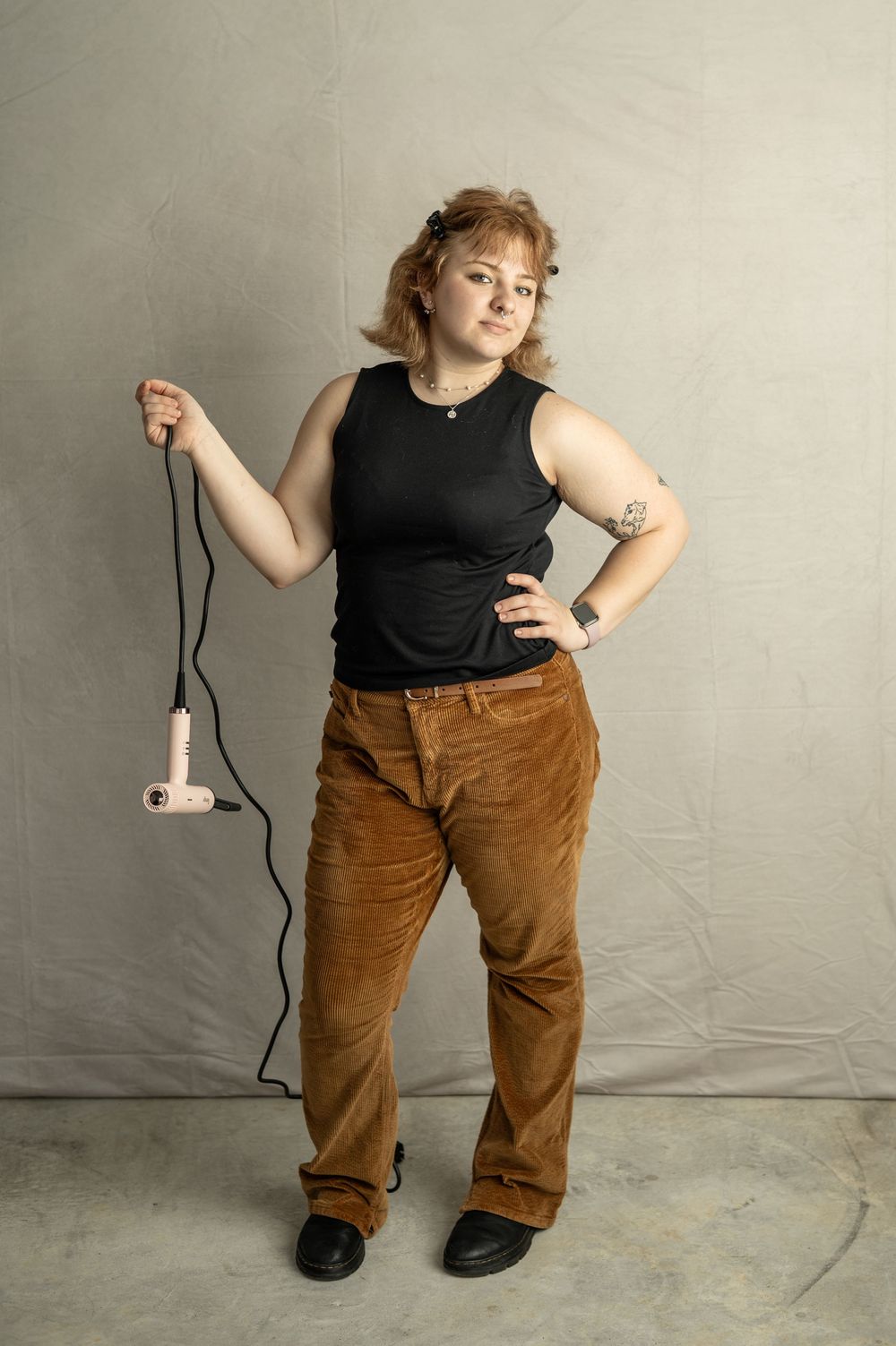 A person wearing a black sleeveless top and brown corduroy pants shows different poses against a white backdrop.