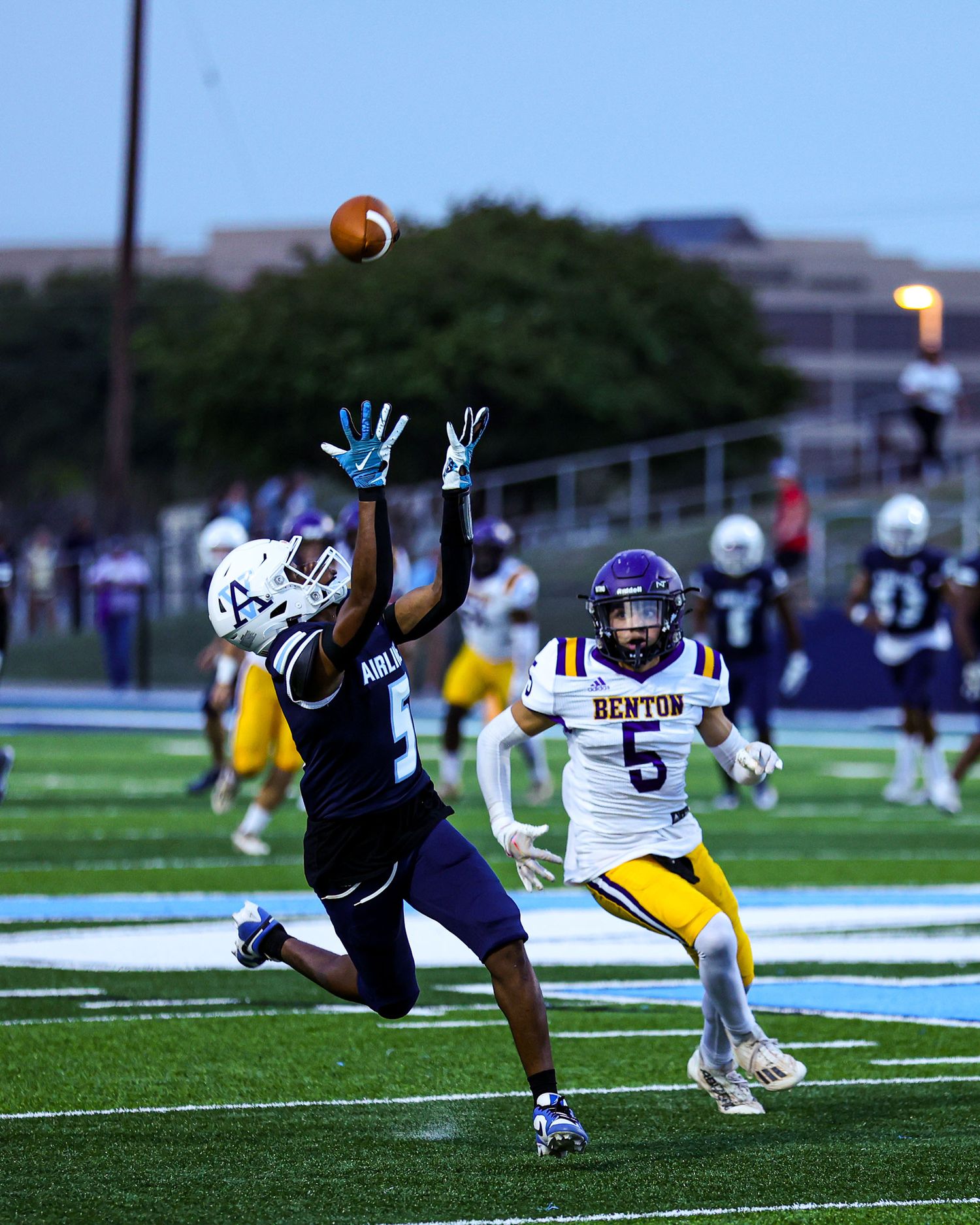 A sequence of wide receiver diving and stretching out to catch a football during a game on an outdoor field at dusk.