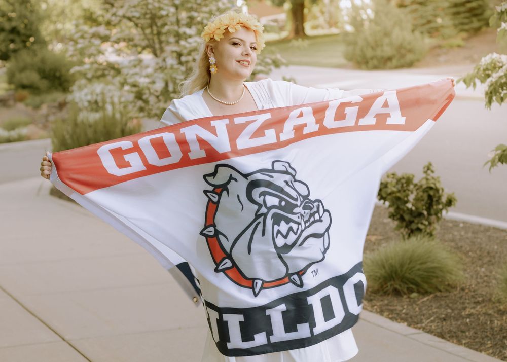 Woman happily holding Gonzaga Bulldogs flag in hand in 60s attire.
