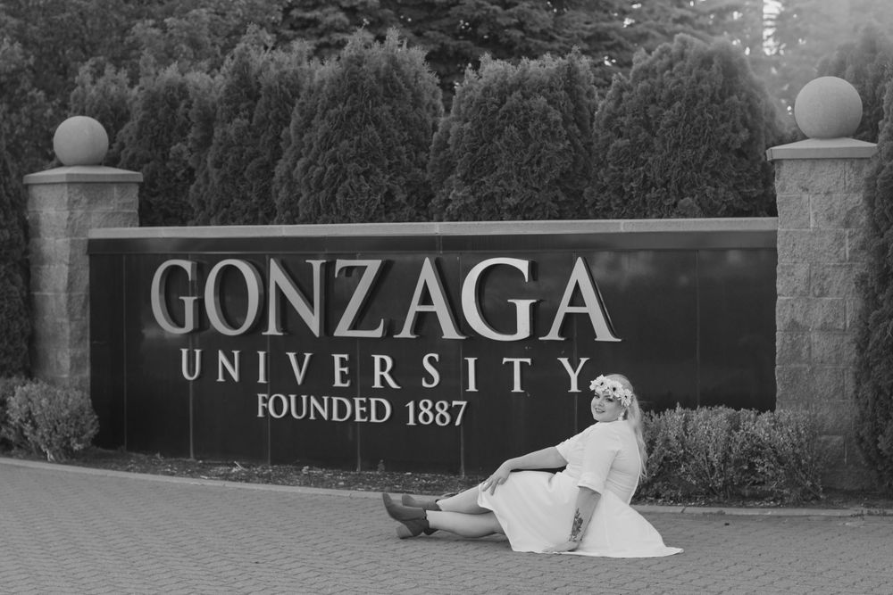College graduate in a sitting pose in front of the Gonzaga University sign, founded in 1887.