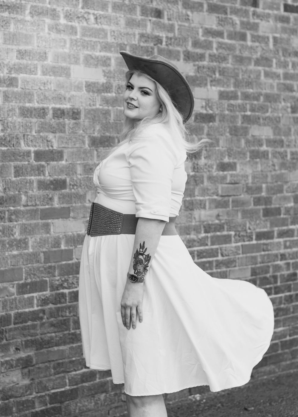 Monochrome photo of woman in cowgirl attire in front of brick wall.