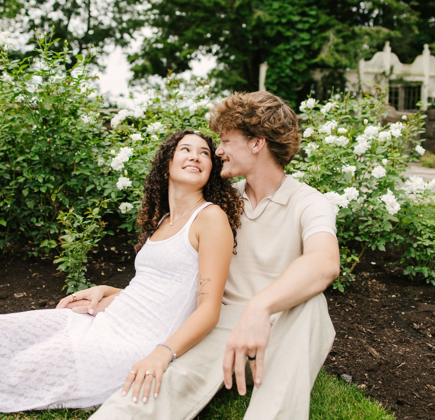 Romantic couple in white outfits lying together in a blooming garden setting.