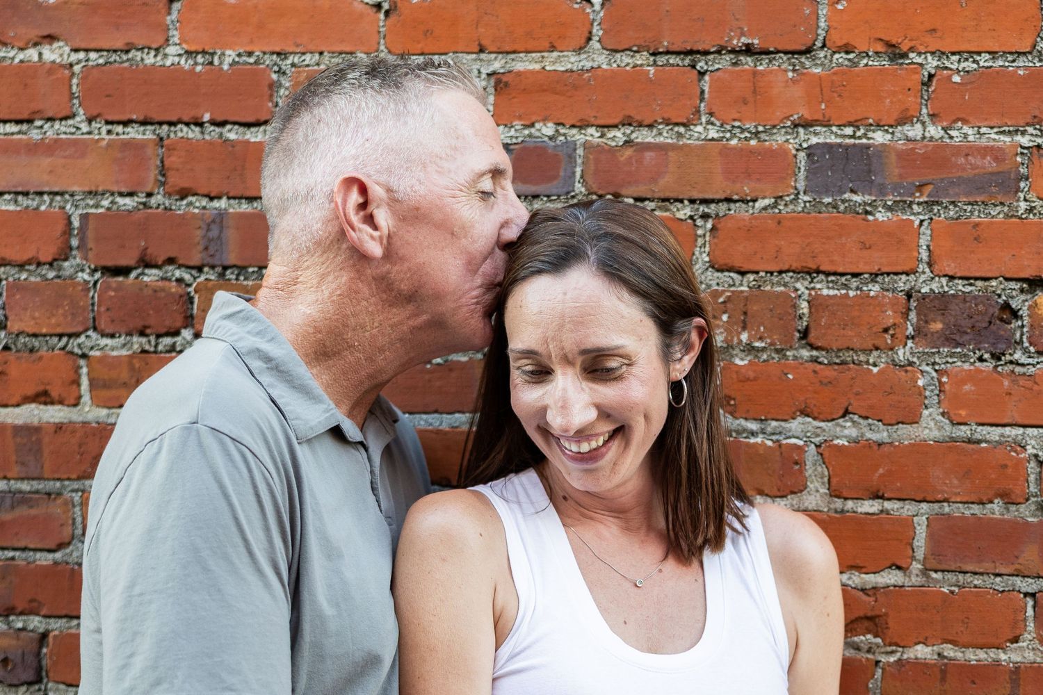 A couple shares a tender moment together against an orange brick wall background.
