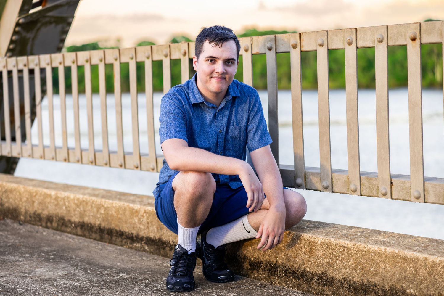 Person in blue shirt sits casually on stone wall next to white railing outdoors.