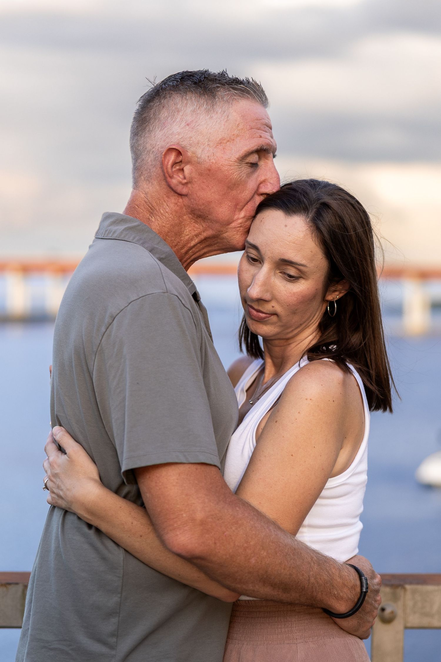 Couple embraces tenderly at sunset near waterfront during romantic outdoor photo session.