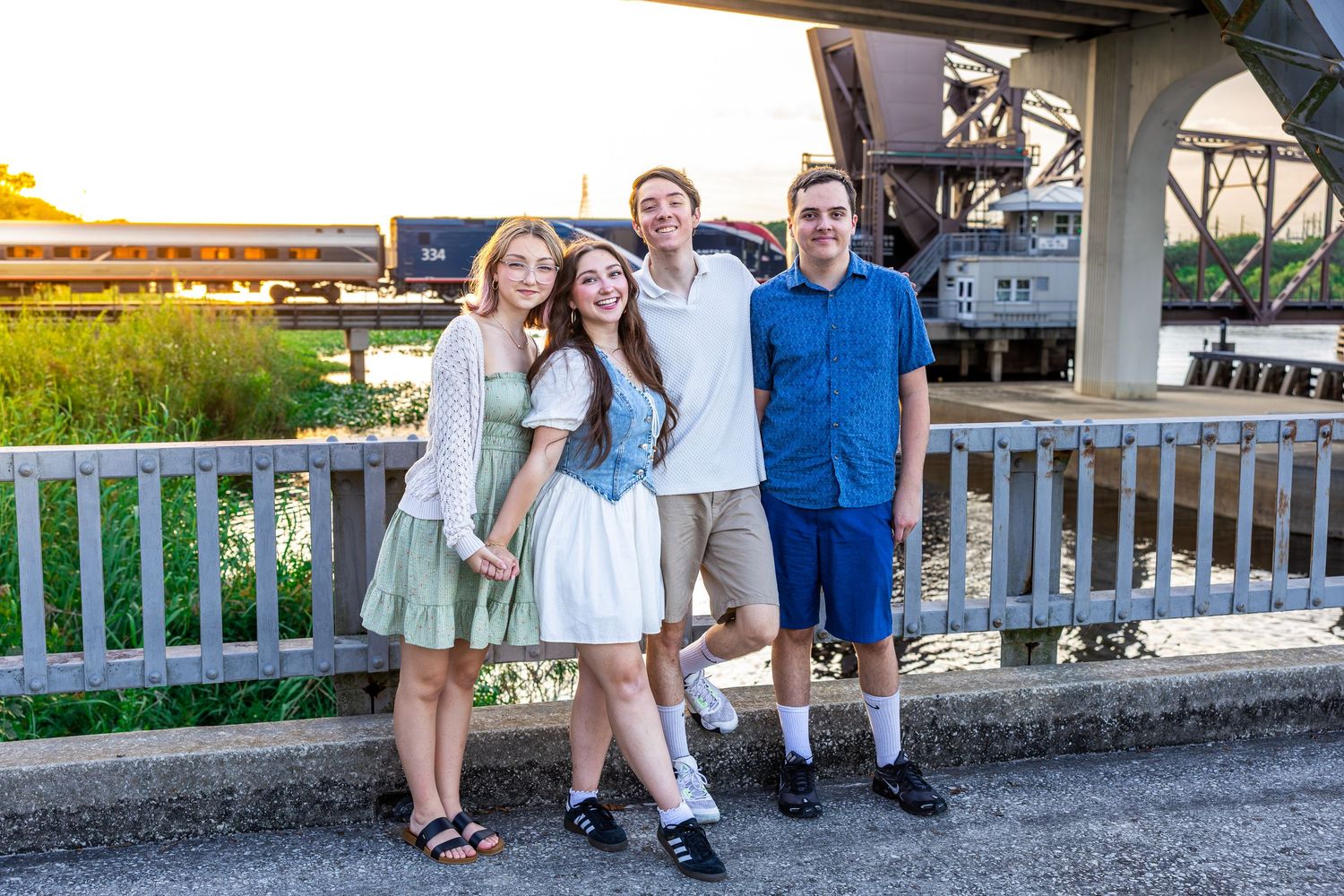 Group in blue and white clothing poses together along a white railing at sunset.