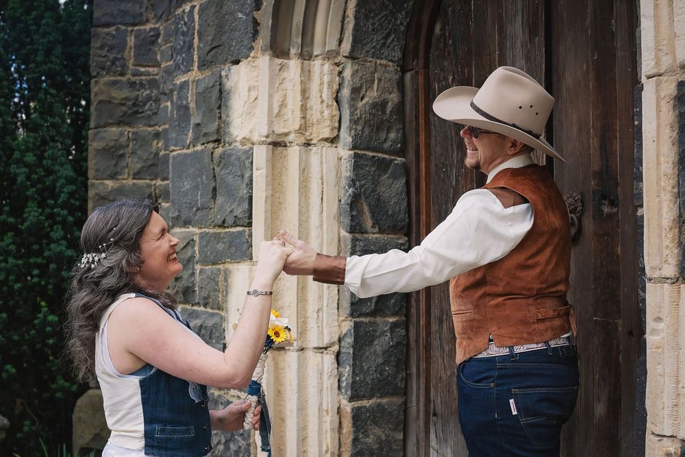 Person in a straw hat and floral dress explores stone archways of historic building exterior with a camera.