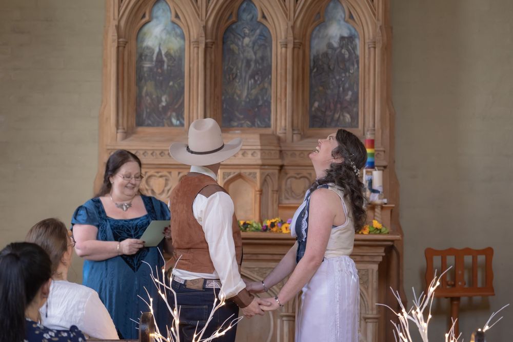 Two figures in formal wedding attire stand in front of an elegant stone archway during their church ceremony.
