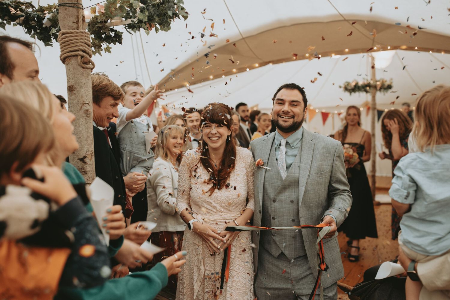 Wedding guests celebrate with confetti throws during an outdoor reception ceremony at sunset.