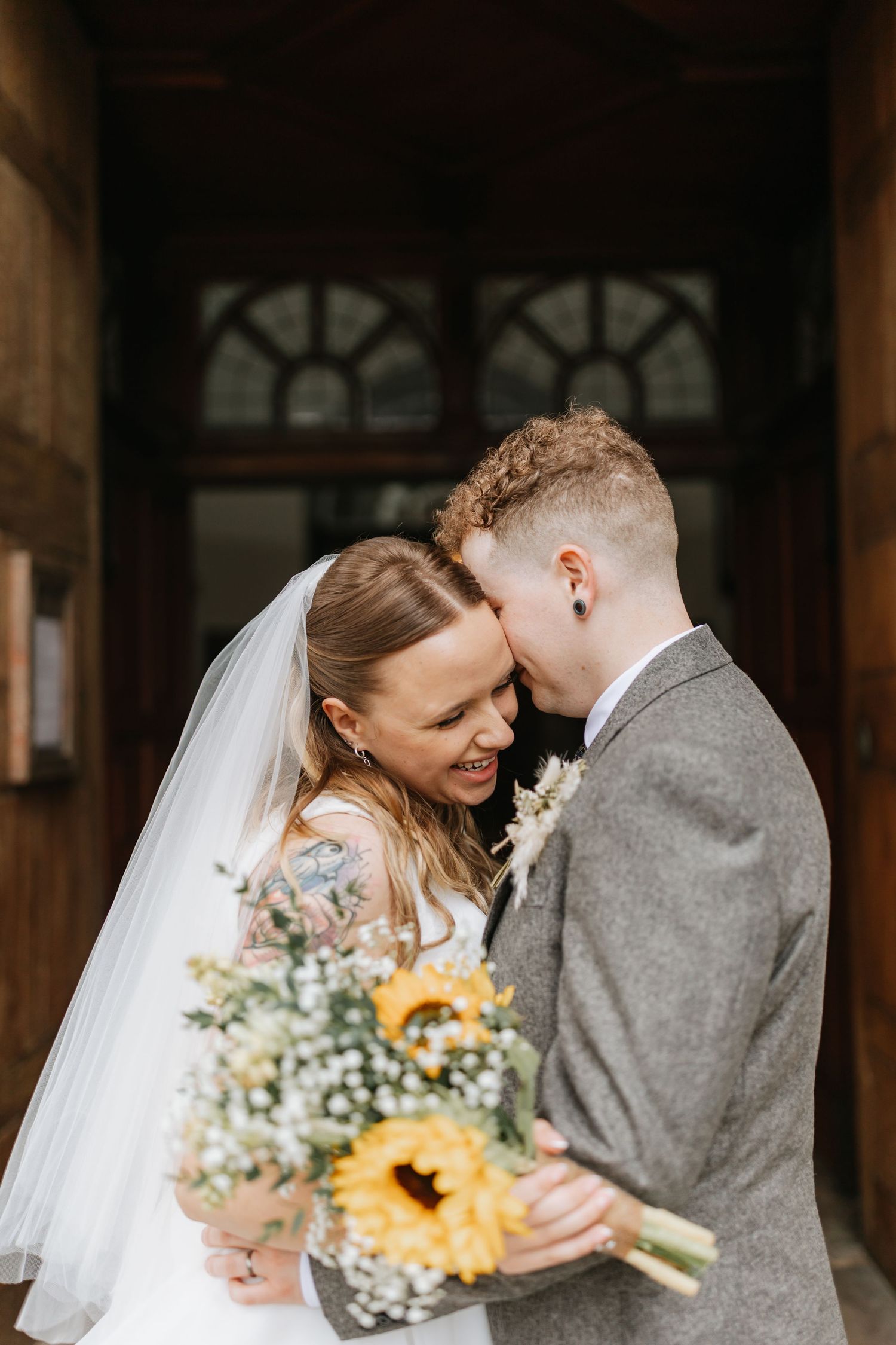 A joyful wedding moment shared between a couple in a grey suit and white dress holding a sunflower bouquet.