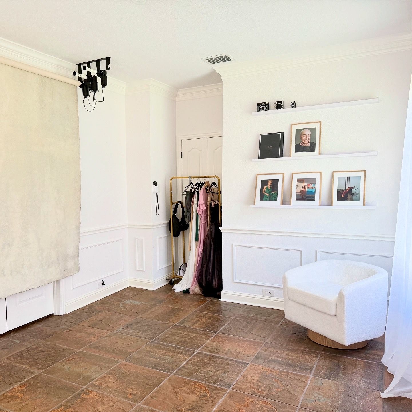 White living room with wainscoting and brown tile flooring connects to a hallway with a built-in storage bench.