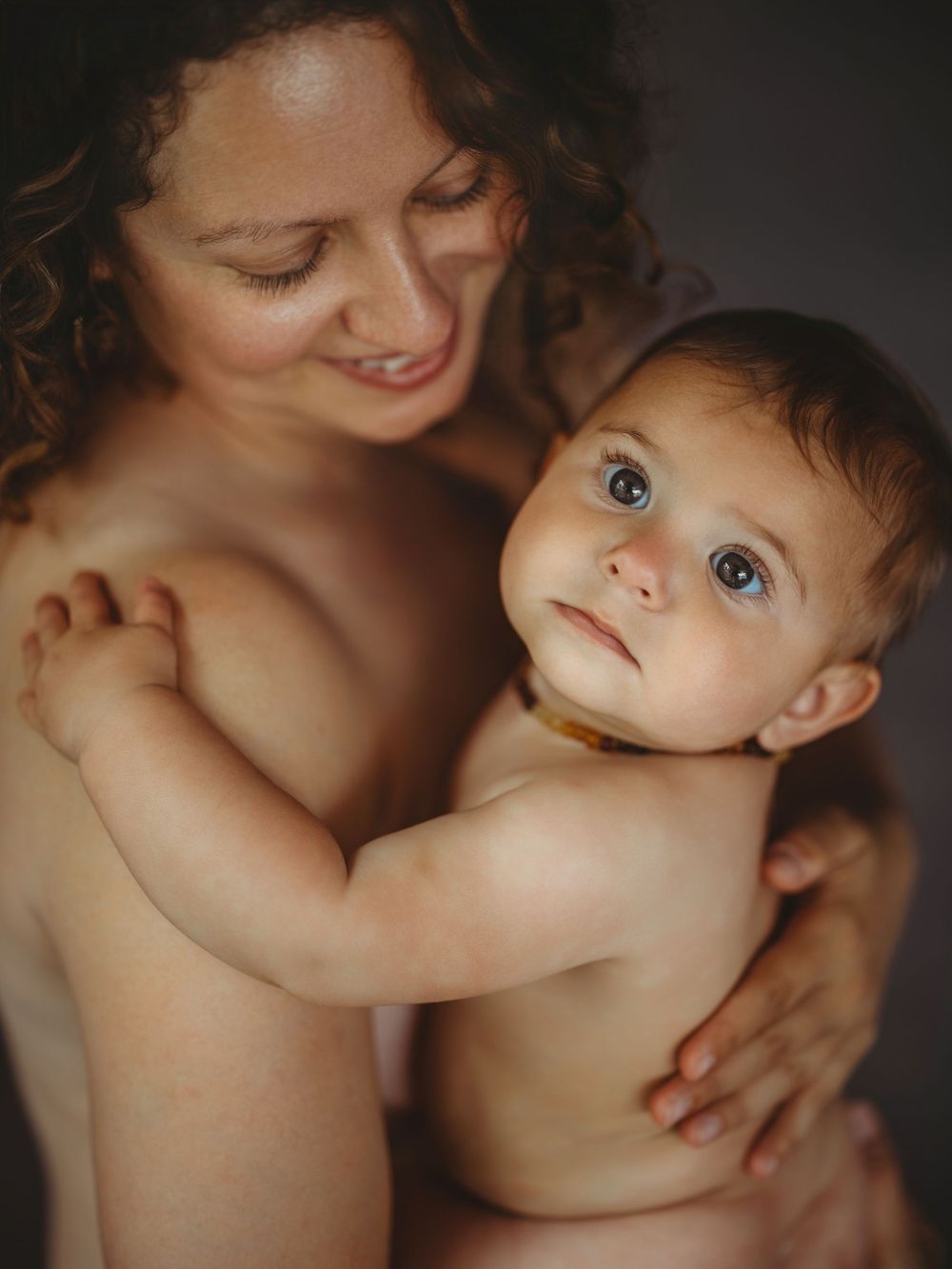 A smiling mother tenderly holds her blue-eyed baby, both sharing a warm and intimate moment together.
