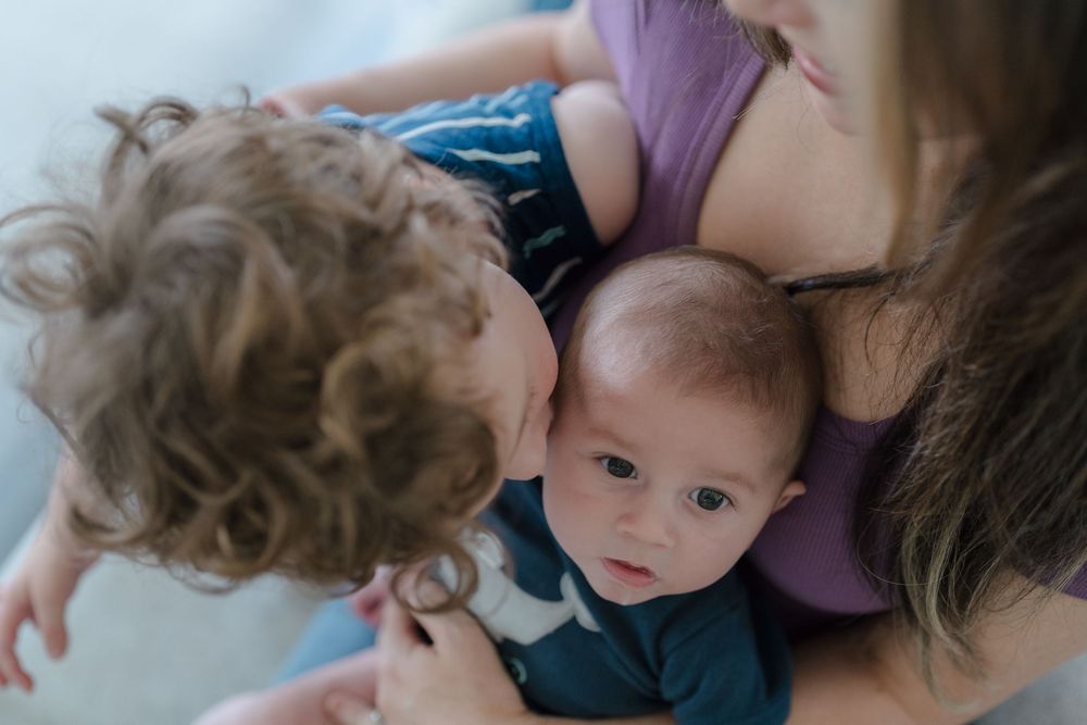 Two small children being held close together while one leans towards the other lovingly at in-home newborn photo session in Kent, Ohio