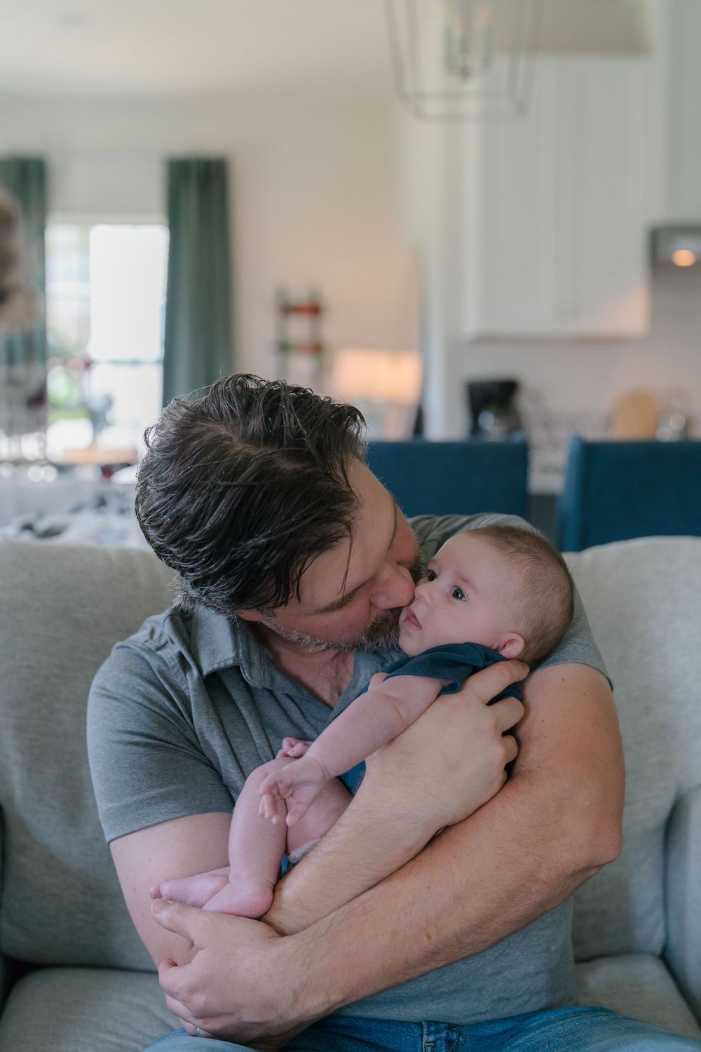 A tender moment between a caregiver and baby as they cuddle on a blue couch in a cozy living room at in-home newborn session in Kent, Ohio