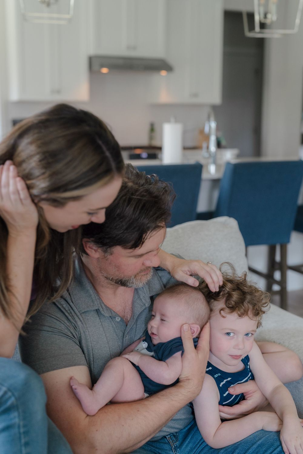 Family shares tender moment together on blue couch in modern kitchen at in-home newborn photo session in Kent, Ohio