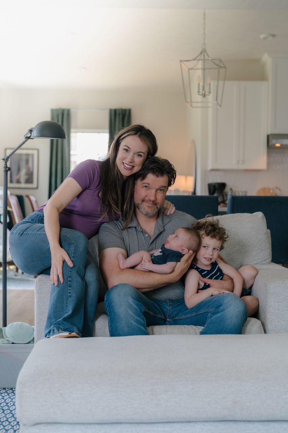 A family relaxes together on a light gray sectional couch in their bright living room at in-home newborn photo session in Kent, Ohio