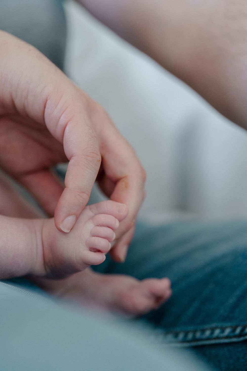 A gentle adult hand touches a tiny baby foot in an intimate close-up photo at in-home newborn photo session in Kent, Ohio