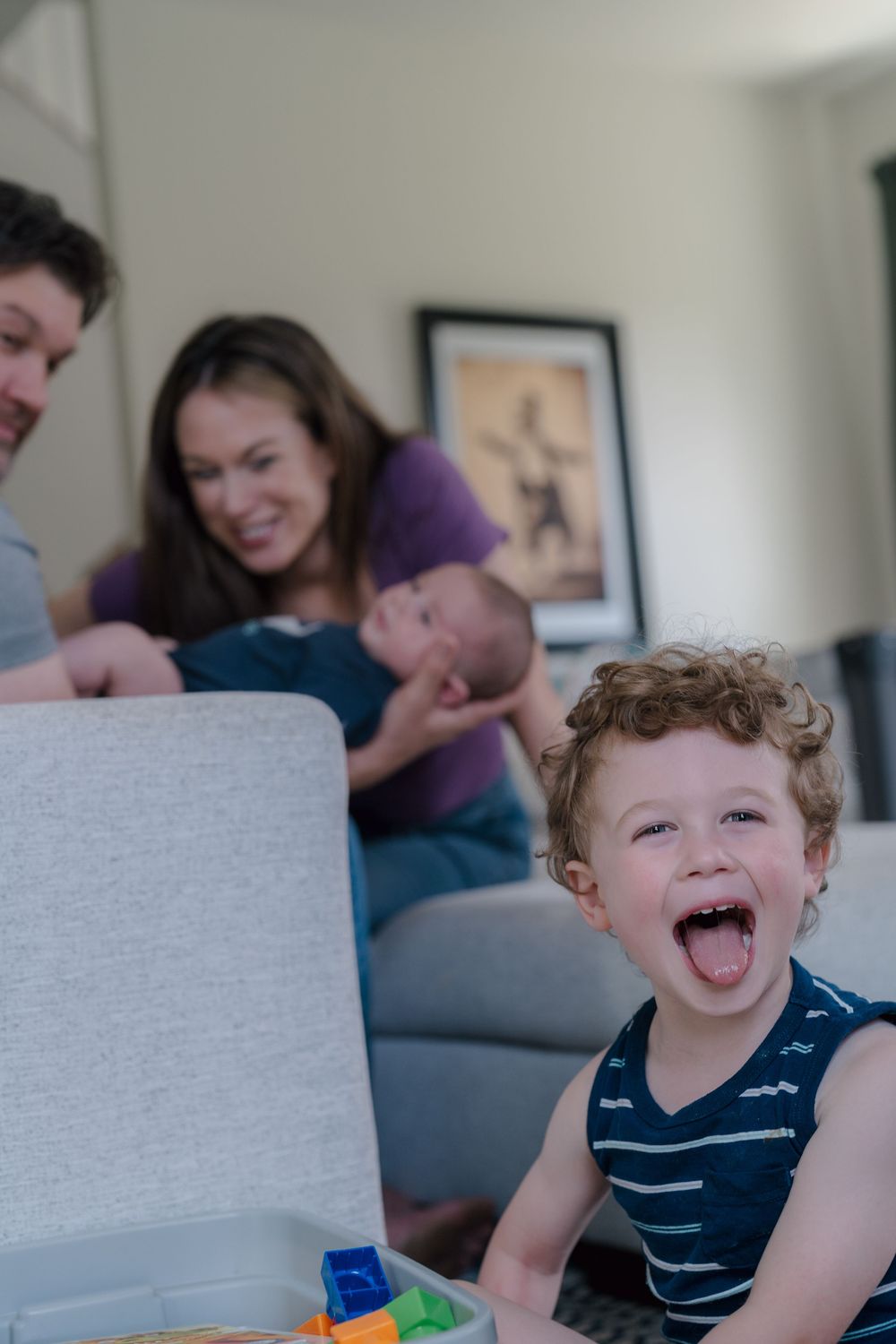 A laughing child with curly hair sits at a table with a joyful expression while wearing a navy striped shirt at in-home photo session in OH