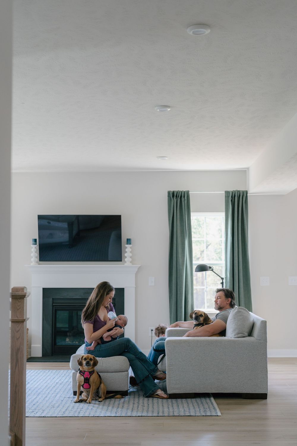 Family relaxes together in a modern living room with green curtains and a fireplace while spending quality time for a newborn session, Kent