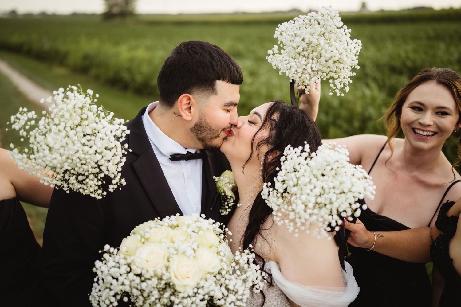 Joyful wedding party laughs together while holding delicate white baby's breath bouquets in an outdoor field setting.