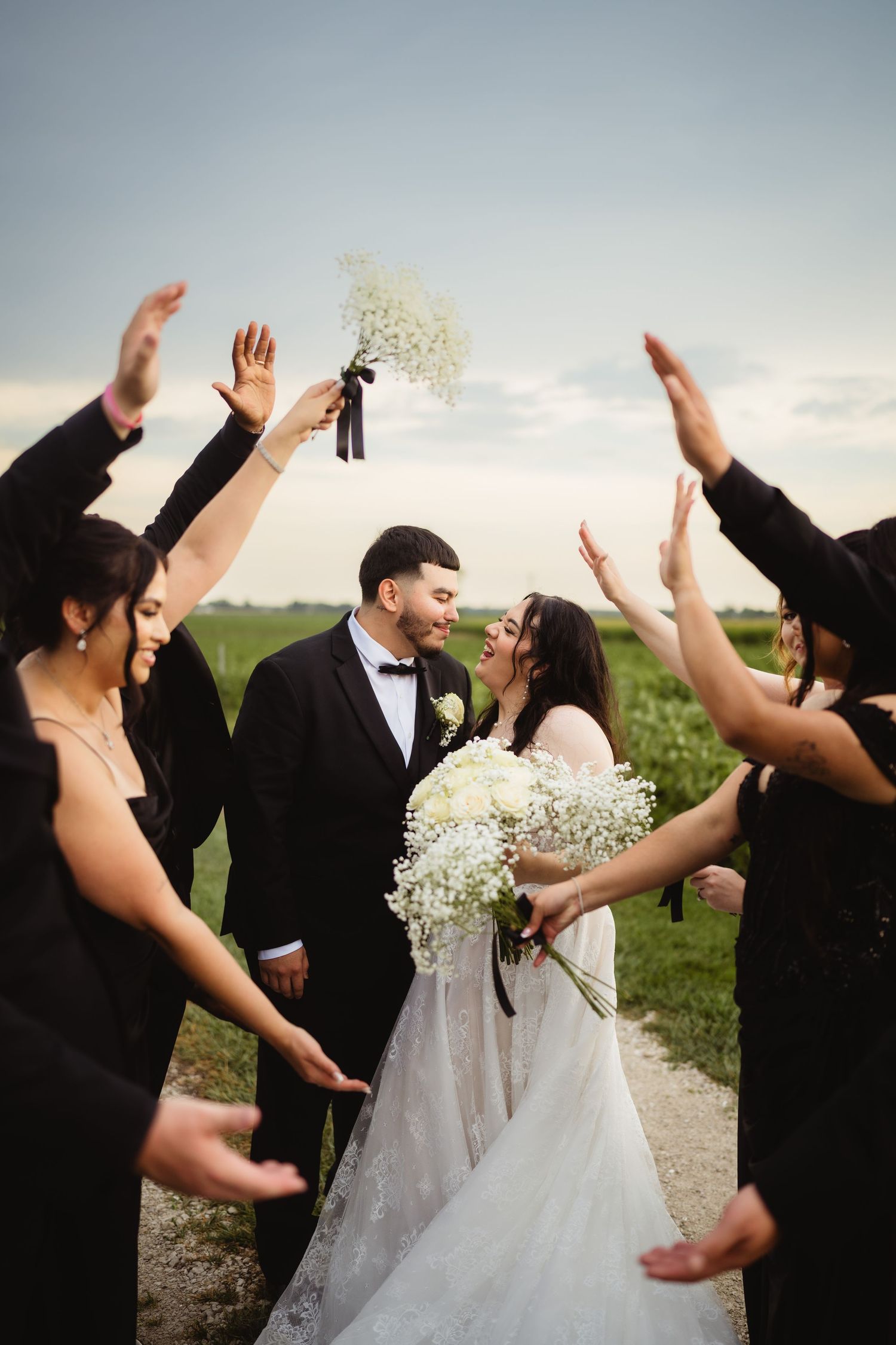 Wedding party celebrates joyfully outdoors as they throw confetti in a grassy field at sunset.