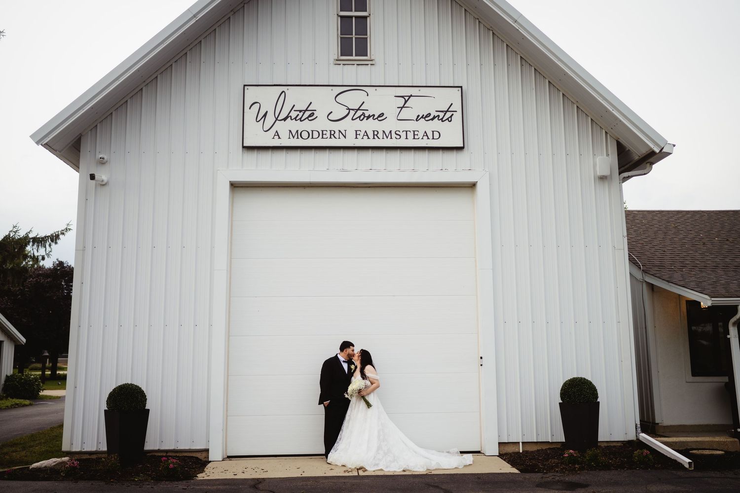 A rustic white barn venue decorated for a wedding ceremony with elegant curtains and white chairs.