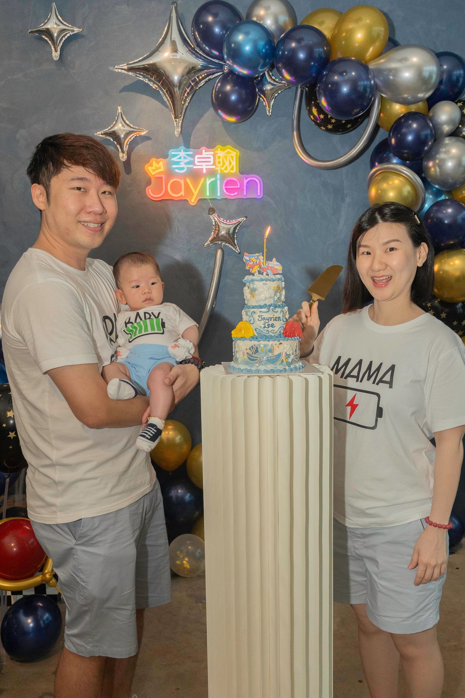 Birthday celebration setup with blue and gold balloon arch, decorative pillar with cake, and color-coordinated party decor.