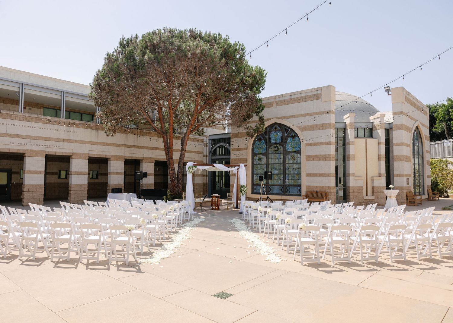 White wedding ceremony setup with rows of chairs facing an archway at an elegant courtyard venue with Mediterranean architecture.