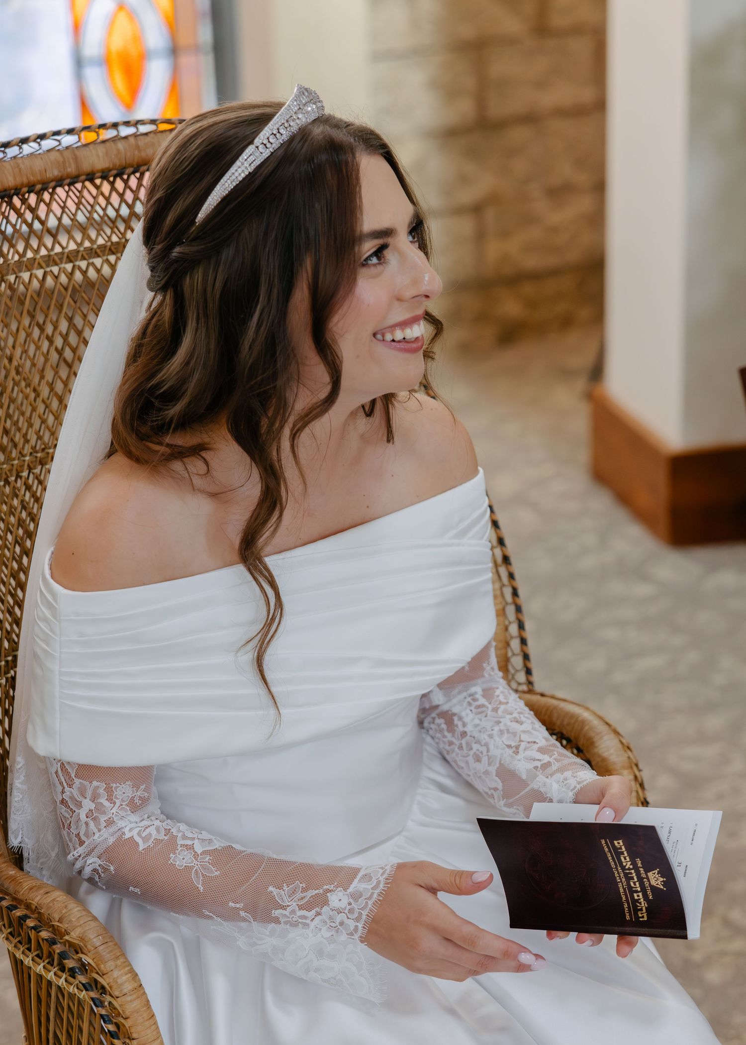 Bride in white lace dress sitting in wicker chair signing ceremony documents.