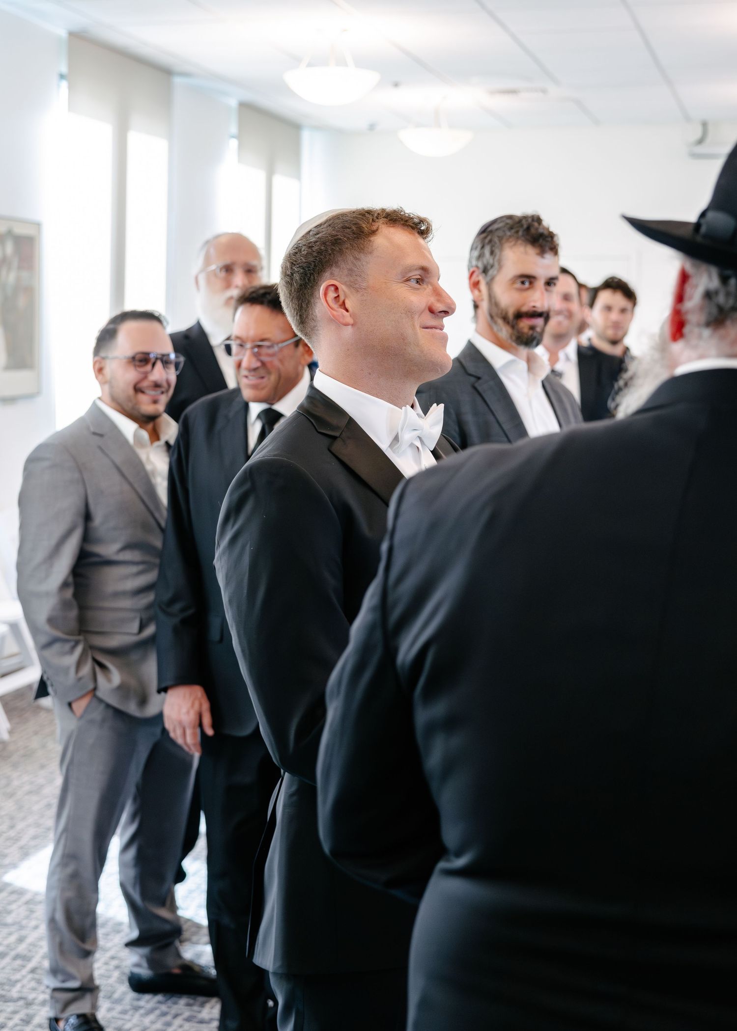 Group of guests and attendees in formal attire gathered at indoor wedding event.