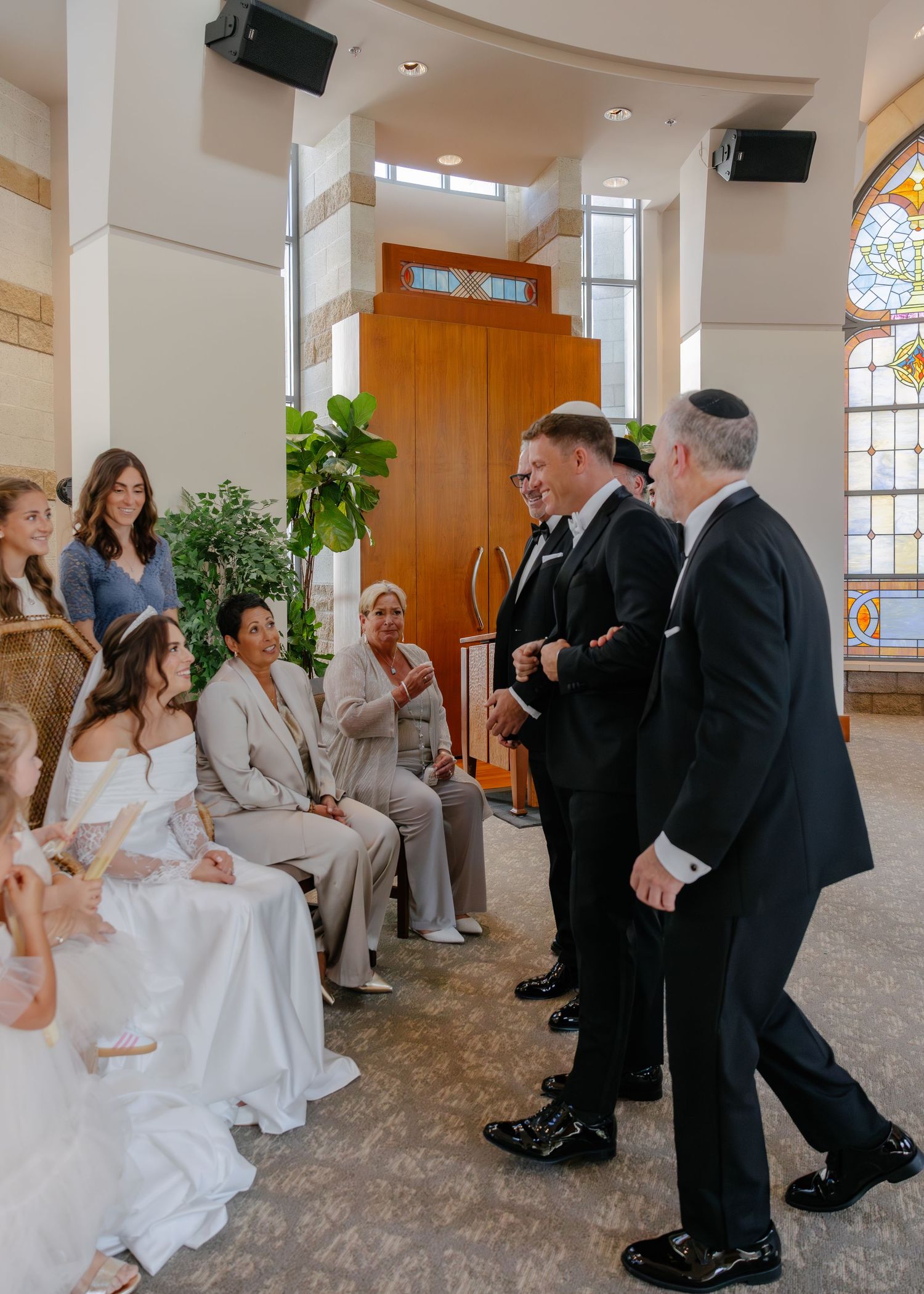 Wedding party members dance and celebrate in an elegant church reception hall.