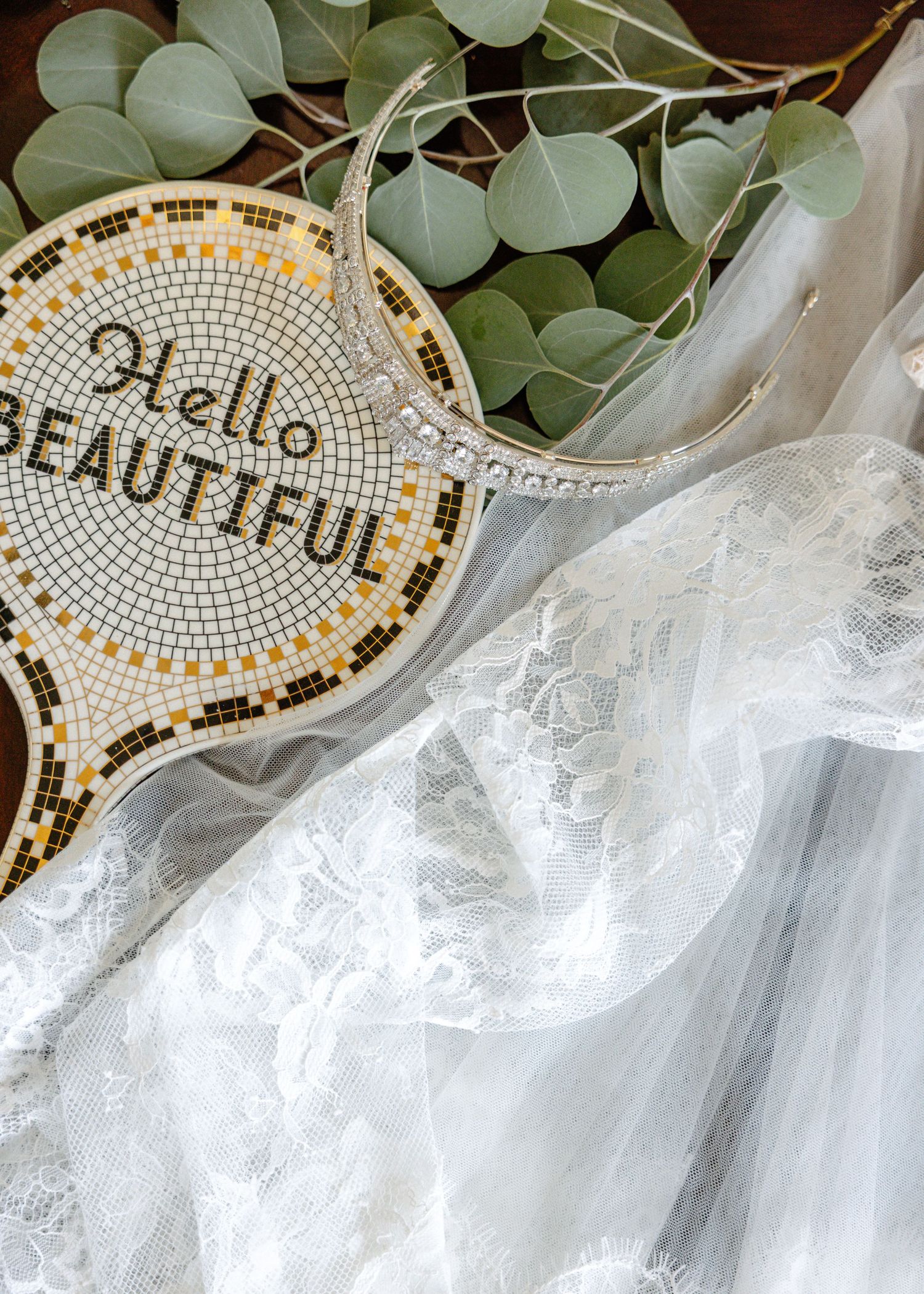 A close-up view of intricate gold and white mosaic lettering designs with soft floral eucalyptus leaves and tulle fabric.
