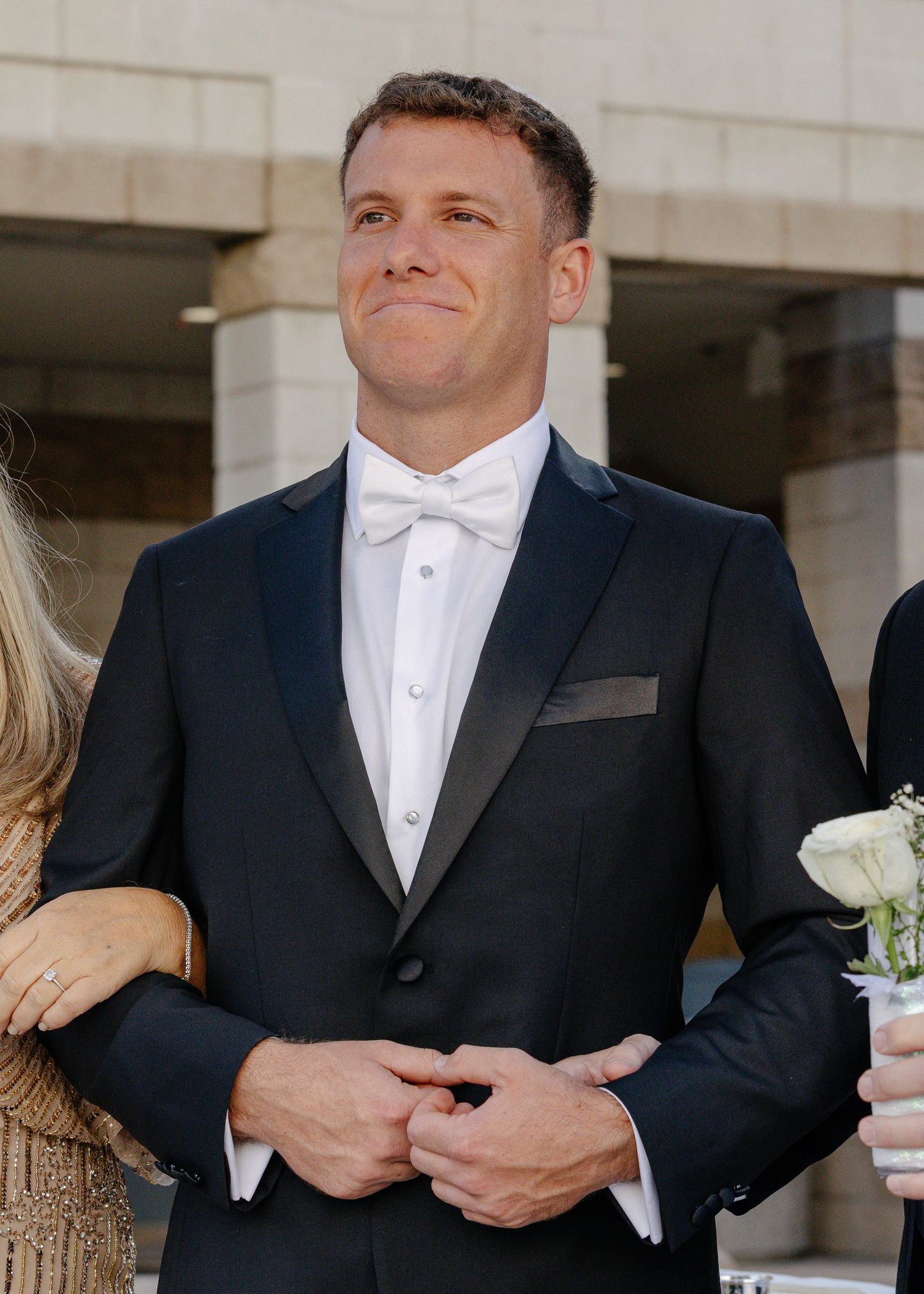 Men in formal black tuxedos with white bow ties stand in line at a formal event.