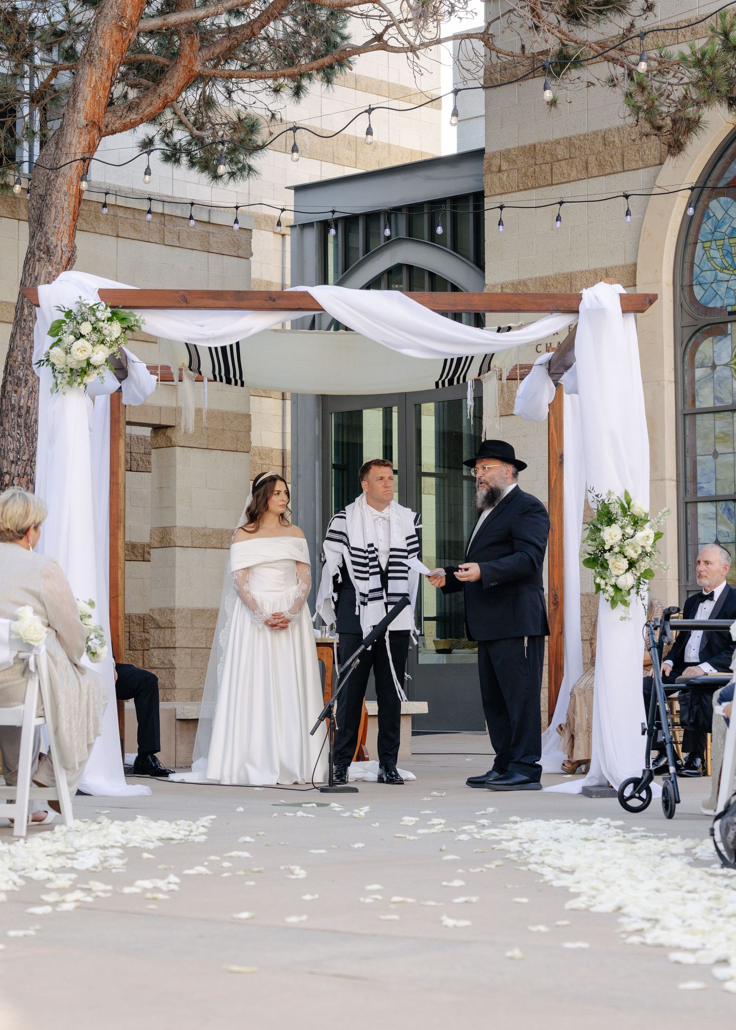 Wedding party stands under pine trees during an outdoor ceremony with white fabric draped between the trees.
