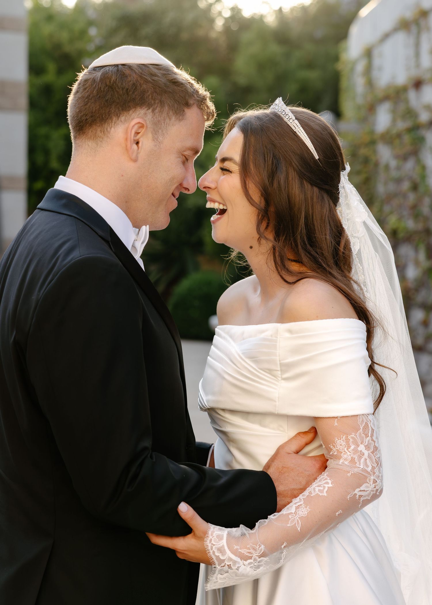 Joyful bride and groom share an intimate moment in their wedding attire during golden hour.