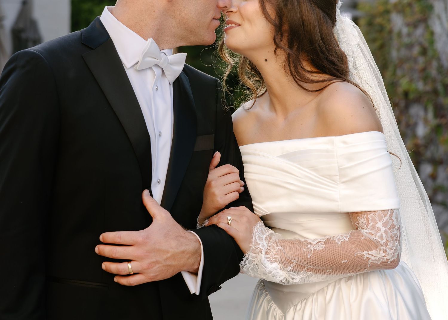 A romantic wedding moment with a couple sharing a kiss, the bride wearing an off-shoulder lace gown with veil.